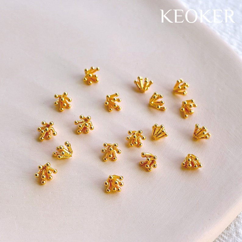 May include: A collection of 15 gold-toned metal bead caps with a starburst design. The bead caps are arranged on a white surface.