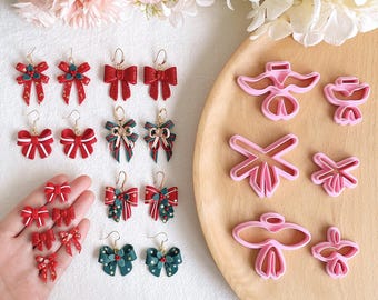 May include: A set of 10 Christmas-themed polymer clay earring molds. The molds are pink and feature various designs, including bows, stars, and angels. The molds are displayed on a wooden surface with a set of red and green Christmas-themed earrings.