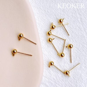 May include: A close-up of ten gold-toned earring findings with a small ball at the end of each post. The findings are scattered on a white surface.