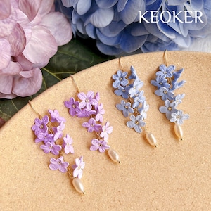 Puede incluir: Dos pares de pendientes colgantes con un racimo de peque&ntilde;as flores moradas y azules. Cada pendiente tiene una sola perla colgando de la parte inferior.