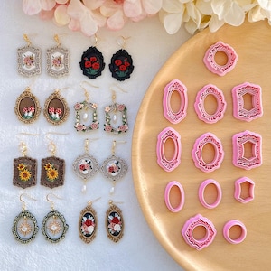 Puede incluir: Una colección de pendientes hechos a mano con diseños florales y enmarcados, con varios colores y formas. Los pendientes se exhiben junto a cortadores de arcilla polimérica rosas con forma de marco en una bandeja de madera.