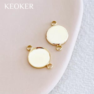 May include: Two gold-colored, round jewelry findings with a blank, cream-colored center. Each finding has three small loops for attaching to other components. The word "KEOKER" is printed in the upper left corner.