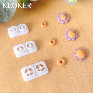 Pode incluir: Tr&ecirc;s moldes de pl&aacute;stico branco com as letras S, M e L, para fazer brincos. H&aacute; tamb&eacute;m tr&ecirc;s pares de brincos em forma de flor roxa e laranja e tr&ecirc;s pequenas pe&ccedil;as em forma de rosquinha laranja.