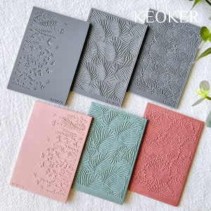 May include: Six silicone stamps with different floral and leaf designs. The stamps are gray, pink, and green. The stamps are labeled "KEOKER".