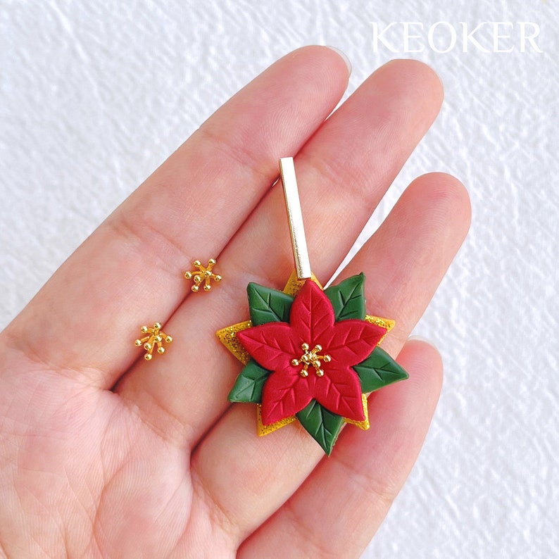 May include: A pair of gold snowflake earrings and a gold and red poinsettia dangle earring. The earrings are handmade and feature a sparkly gold finish.