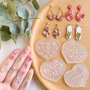 May include: Four heart-shaped silicone molds for making polymer clay earrings. The molds feature different designs: butterflies, flowers, tulips, and leaves. There are also six pairs of polymer clay earrings with floral designs.