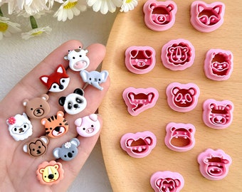 May include: A set of 16 pink plastic cookie cutters shaped like various animals, including a bear, fox, panda, tiger, elephant, koala, and more. The cutters are arranged on a wooden surface.