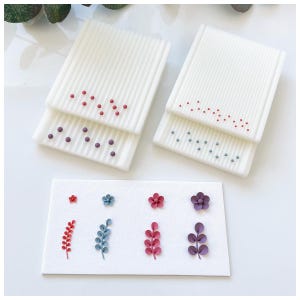 Puede incluir: Objetos rectangulares blancos con superficies acanaladas y diseños punteados en rojo, morado y azul. Debajo, un rectángulo blanco muestra diseños florales y de hojas en miniatura en rojo, azul y morado, para manualidades.