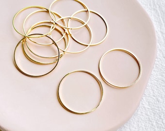 May include: A group of ten gold-colored metal hoops of varying sizes on a pink surface. The word "KEOKER" is printed in black on the surface.
