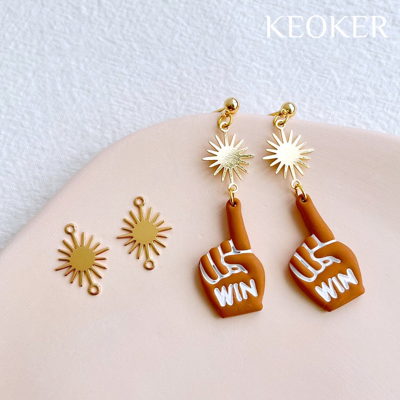 May include: Gold tone earrings with a star charm and a brown hand charm with the word "WIN" written on it.