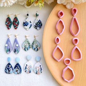 May include: A set of 10 polymer clay earrings and 5 cookie cutters. The earrings feature floral designs in shades of blue, green, and purple. The cookie cutters are pink and shaped like teardrops and a hexagon.
