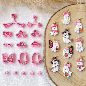 May include: A collection of pink plastic cookie cutters and matching polymer clay ghost earrings. The cutters feature shapes like bows, hats, and butterflies. The earrings depict white ghosts with various accessories including pink bows, witch hats, and butterfly wings.