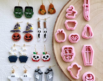 May include: A collection of Halloween-themed earrings and cookie cutters. The earrings feature designs like Frankenstein's monster, pumpkins, ghosts, and coffins. The cookie cutters are in the shapes of a knife, ghost, pumpkin, and apple. The earrings are on gold hoops.