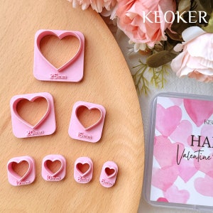 May include: Set of 7 pink heart-shaped cookie cutters in various sizes, ranging from 5 mm to 25 mm. The cutters are arranged on a wooden surface. The background includes a box with a pink watercolour design and the text "Happy Valentine's Day".