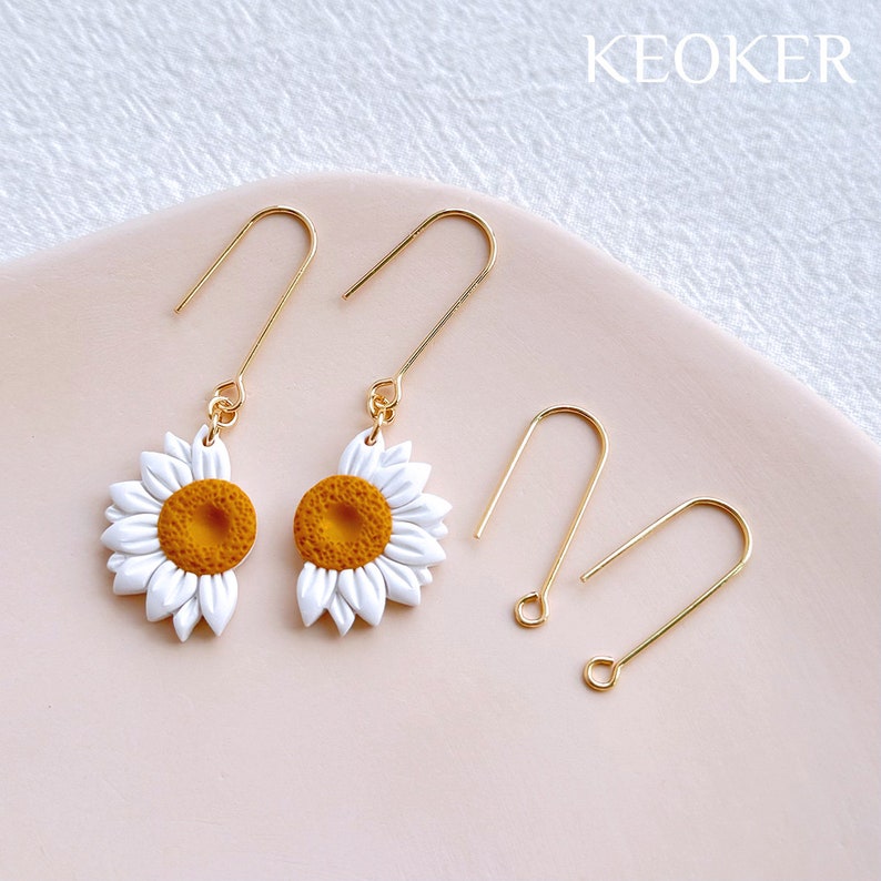 Peut inclure: Une paire de boucles d'oreilles pendantes dor&eacute;es avec des breloques de tournesol blancs et jaunes. Les boucles d'oreilles sont pr&eacute;sent&eacute;es avec des crochets d'oreilles dor&eacute;s suppl&eacute;mentaires.