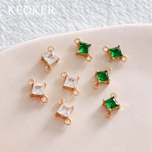 May include: Gold-coloured jewellery findings with square-cut, clear and emerald green gemstones. The findings are diamond-shaped with small loops on each corner for attaching to other jewellery components. The word "KEOKER" is printed in the top left corner.