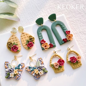 May include: A set of six pairs of floral earrings. The earrings are made of polymer clay and feature a variety of designs, including butterflies, baskets, and arches. The earrings are all decorated with colorful flowers and leaves.
