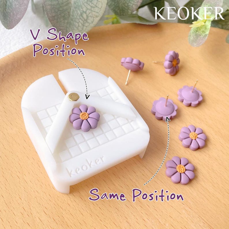Pode incluir: Uma ferramenta de pl&aacute;stico branco com um padr&atilde;o de grade e a palavra "keoker" impressa nela. A ferramenta &eacute; usada para ajudar a posicionar brincos. Existem v&aacute;rios brincos em forma de flor roxa com centros amarelos sobre uma superf&iacute;cie de madeira.