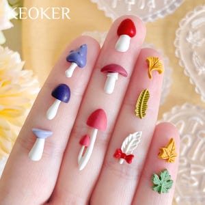 May include: A hand model displays a variety of colorful miniature mushroom and leaf charms. The charms are made of polymer clay and have a variety of colors and designs.