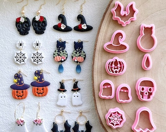 May include: A collection of Halloween-themed earrings and cookie cutters. The earrings feature designs like skulls, witch hats, pumpkins, ghosts, spiders, and bats. The cookie cutters are pink and include shapes of bats, witch hats, pumpkins, ghosts, and a spider web.