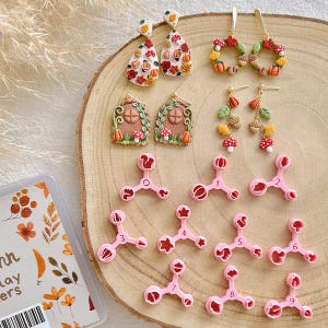 Puede incluir: Una colección de pendientes y cortadores de arcilla polimérica hechos a mano. Los pendientes presentan diseños con temática otoñal como calabazas, setas y hojas. También se ven cortadores rosas de varias formas, junto con un recipiente transparente con diseños florales.