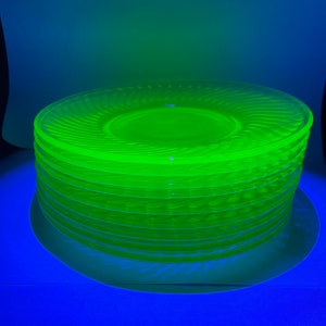 May include: A stack of ten bright yellow-green glass plates with a swirl design. The plates are stacked on a blue surface.