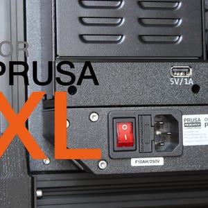 May include: A close-up of a black Prusa XL 3D printer component. The image shows a power switch, a power inlet, and a USB port labelled 5V/1A. The text "FOR PRUSA XL" is displayed in black and orange.