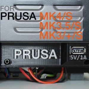 May include: A black 3D printer component featuring the word "PRUSA" in white. It includes a USB port marked "5V/1A" and is designed for MK4/S, MK3.5/S, and MK3/+S models.