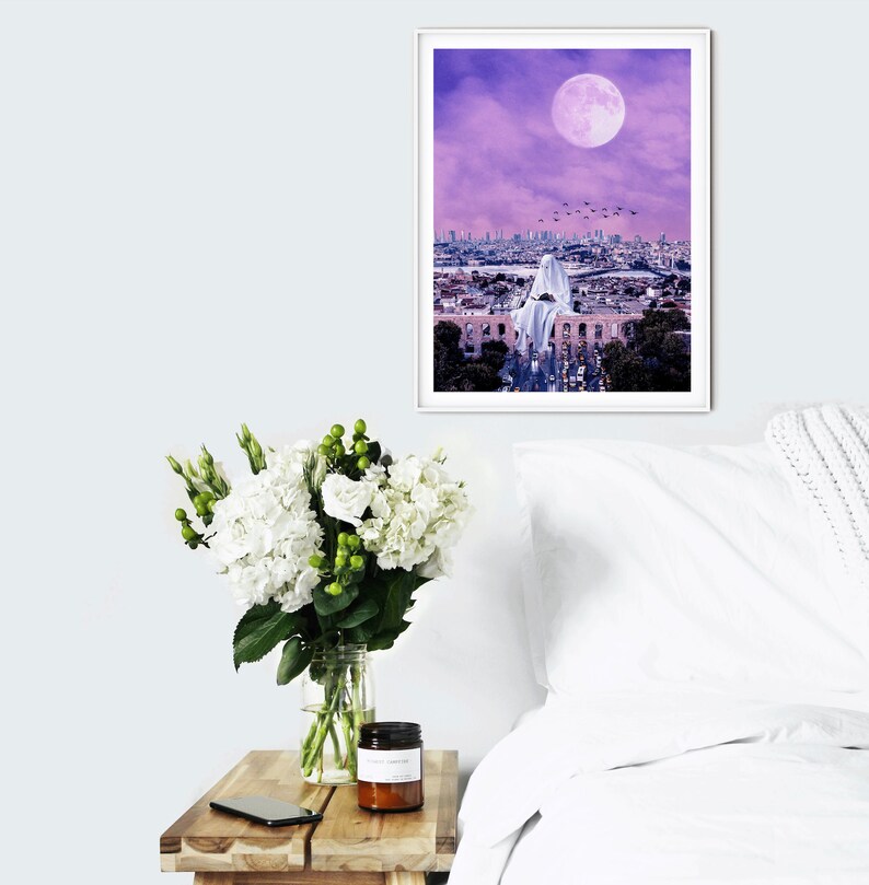 May include: A framed print of a city skyline at night with a large, full moon in the sky. A white figure is sitting on a building in the foreground. The sky is a vibrant purple color.