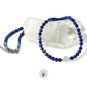 May include: A blue lapis lazuli beaded necklace with a clear crystal charm. The necklace is on a white background.