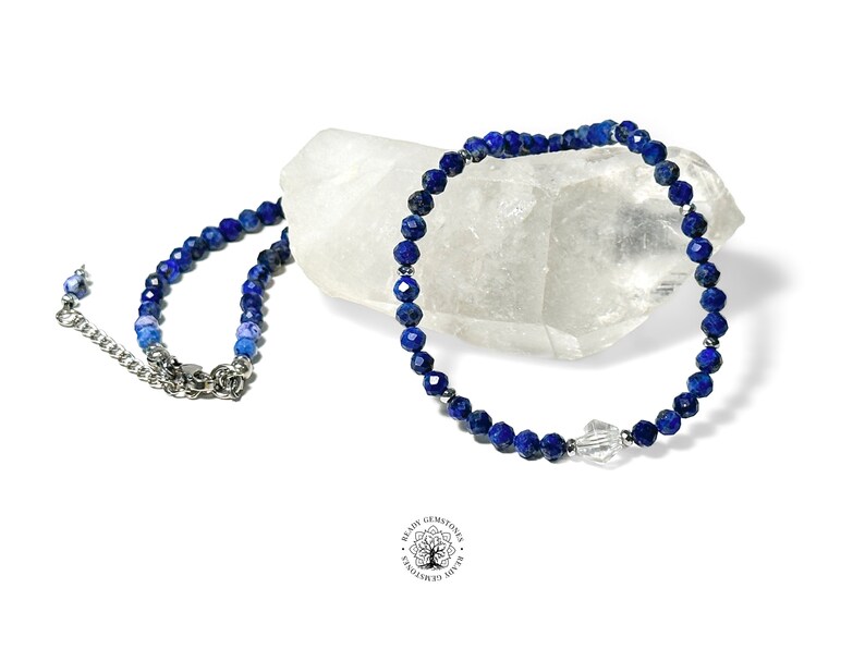 May include: A blue lapis lazuli beaded necklace with a clear crystal charm. The necklace is on a white background.