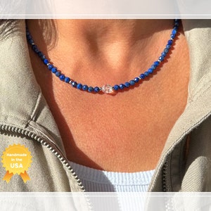May include: A delicate necklace made with small blue lapis lazuli beads and a clear crystal pendant. The necklace is handmade in the USA.