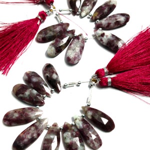 May include: A strand of pink and white gemstone beads with a teardrop shape. The beads are strung on silver wire with silver spacers. The strand is finished with two pink tassels.