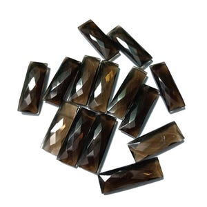 May include: A group of 12 faceted smoky quartz stones in a rectangular shape. The stones are a dark brown color and have a glossy finish.