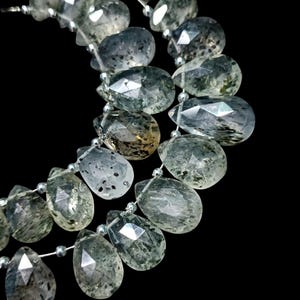 May include: Close-up of strands of faceted, teardrop-shaped gemstones in green and clear hues. The beads are strung on silver-coloured wire, suitable for jewellery making. The gemstones have inclusions and a polished finish.