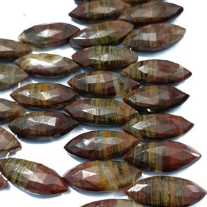 May include: A selection of faceted, oval gemstones. The stones exhibit a blend of earthy tones, such as deep reds, browns, and touches of green and yellow. The cut of the stones creates multiple reflective surfaces, enhancing their natural patterns.