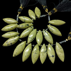 May include: A strand of light green and black marbled gemstone beads, each bead is a marquise shape. The beads are strung on a silver wire with silver spacers between each bead. The strand is finished with black tassels on each end.