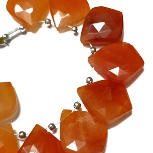 Könnte beinhalten: Eine Kette aus Karneol-Edelsteinen, jede Perle ist facettiert und hat eine einzigartige Farbvariation in Orange und Rot. Die Perlen sind auf einem Silberdraht aufgefädelt.