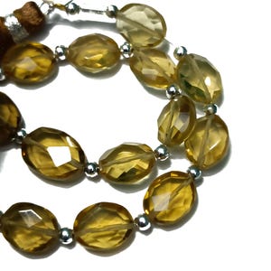 May include: A strand of oval-shaped, faceted, golden brown gemstone beads with silver spacers. The beads are strung on a silver wire.