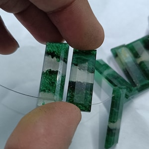 May include: Rectangular green and white gemstone beads. The beads are faceted with a clear, transparent appearance. The green color has a marbled effect. The beads are strung on a thin, clear wire.