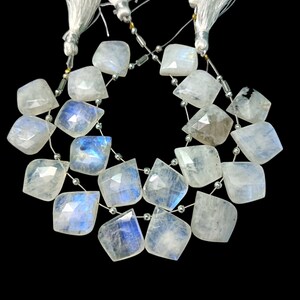 Peut inclure: Un collier de perles de pierre de lune blanche avec un éclat nacré. Les perles sont facettées et ont une forme de larme. Le collier est enfilée sur un fil d'argent et a des glands blancs à chaque extrémité.