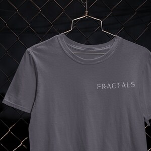 May include: A gray t-shirt with the word "FRACTALS" printed in white on the front. The shirt is hanging on a metal hanger against a chain link fence.