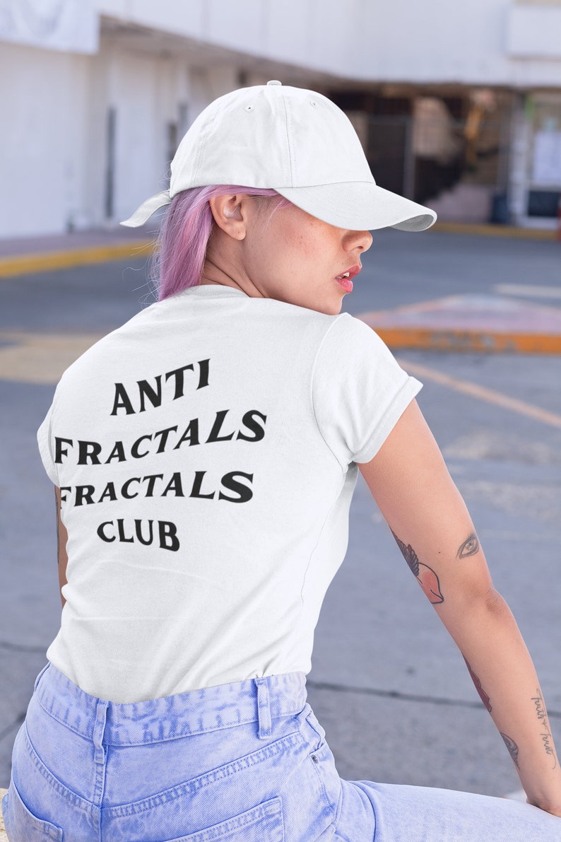 May include: A white t-shirt with black text that reads "ANTI FRACTALS FRACTALS CLUB". The person wearing the shirt has pink hair and is wearing a white baseball cap.