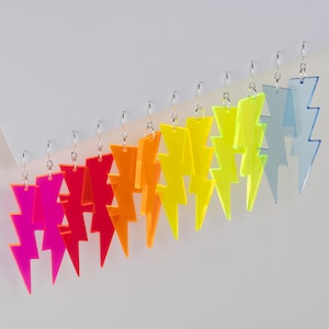 May include: A set of 10 pairs of neon lightning bolt earrings. The earrings are made of acrylic and come in a variety of colours, including pink, orange, yellow, green, blue, and purple.