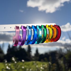 Könnte beinhalten: Ein Satz Regenbogen-Hoop-Ohrringe. Die Ohrringe sind aus klarem Acryl und in Regenbogenreihenfolge angeordnet, von Lila bis Rot.