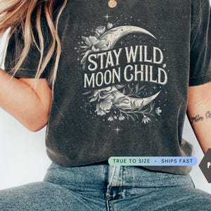 May include: A dark gray t-shirt with a crescent moon and floral design. The text "Stay Wild Moon Child" is printed on the shirt.