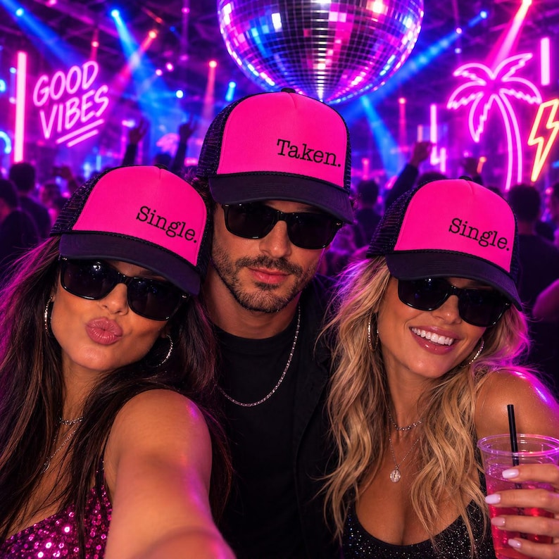 Puede incluir: Tres gorras de camionero de color rosa ne&oacute;n y negro con el texto 'Single.' en dos gorras y 'Taken.' en la gorra central. Cada gorra tiene una parte trasera de malla y un panel frontal s&oacute;lido. Las gorras son usadas en una discoteca.