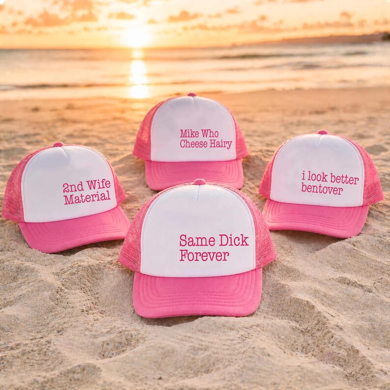 Puede incluir: Cuatro gorras tipo camionero en rosa y blanco con parte trasera de malla. Las gorras tienen texto en rosa: 2nd Wife Material, Mike Who Cheese Hairy, i look better bentover y Same Dick Forever. Cada gorra tiene un panel frontal blanco y visera rosa.