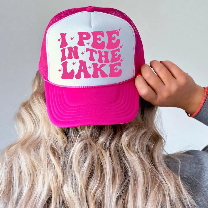 a woman wearing a pink and white trucker hat with i pee in the lake