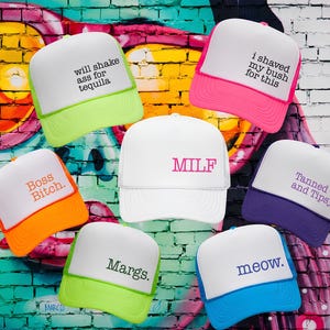 Puede incluir: Siete gorras de camionero de espuma con paneles frontales blancos y viseras de colores. El texto incluye: will shake ass for tequila, i shaved my bush for this, Boss Bitch., MILF, Tanned and Tipsy, Margs., y meow. en varios colores y estilos.